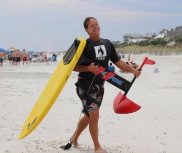a man carrying a surfboard on top of a sandy beach