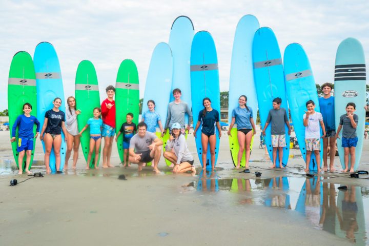 Group of people in swimsuits posing with surfboards on a beach.