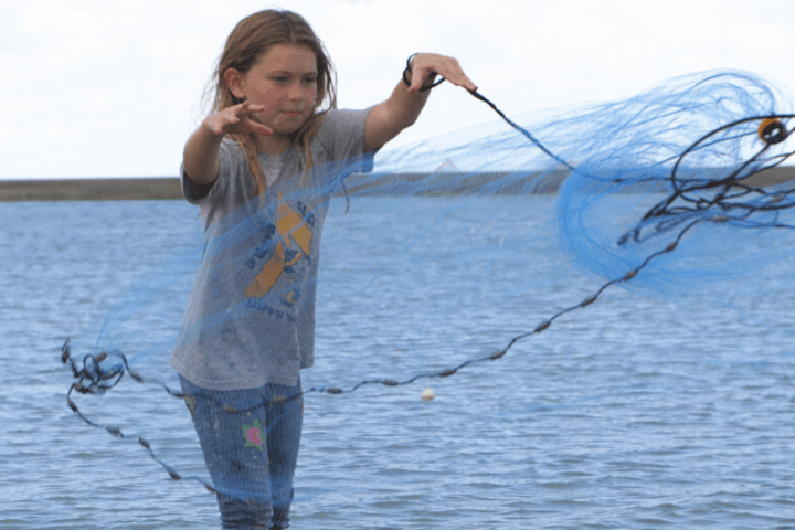 Child throwing a fishing net over water on a sunny day.