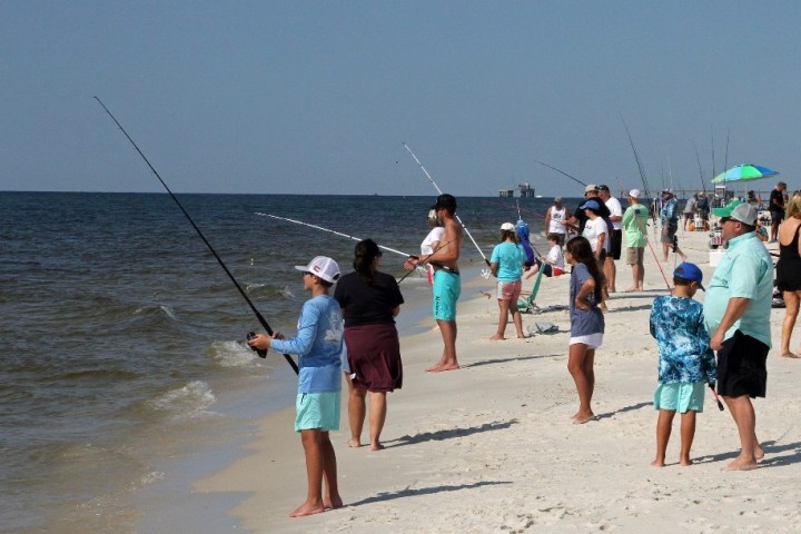 People fishing along a sandy beach with the ocean in the background.
